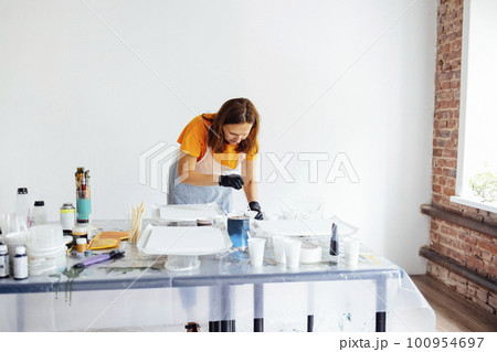 Painting tutorial. White woman in the gloves paint with liquid acrylic in an art workshop 100954697