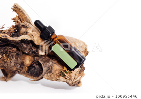 Mock up of brown serum or oil glass bottle with pipette and green sticker lies on wooden snag or part of tree root. Mock up of brown serum or oil glass bottle with pipette and green sticker lies on wooden snag or part of tree root. 100955446