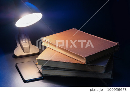 A stack of old books and table lamp on a dark background A stack of old books and table lamp on a dark background 100956673
