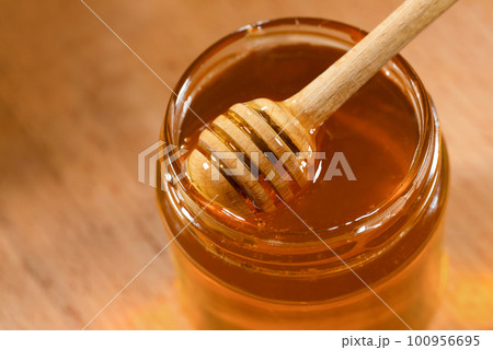 Wooden ladle with honey and a glass jar, on a wooden table close-up. Organic beekeeping products 100956695