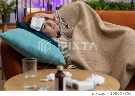 Sick ill woman suffering from cold or allergy sitting on home sofa sneezes wipes snot into napkin 100957756