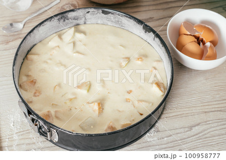 Baking dish with raw apple pie dough stands on kitchen counter next to bowl with eggshells 100958777