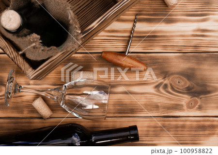 Wine glass, corkscrew, corks, wine bottles, grapevine on rustic burnt wooden background. Top view. Copy space 100958822