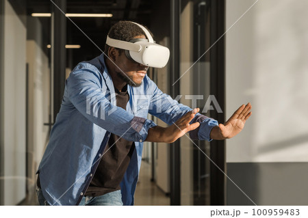 Man in vr headset exploring metaverse world, touching virtual reality subjects. Abstract cyber world in office Man in vr headset exploring metaverse world, touching virtual reality subjects. Abstract cyber world in office 100959483