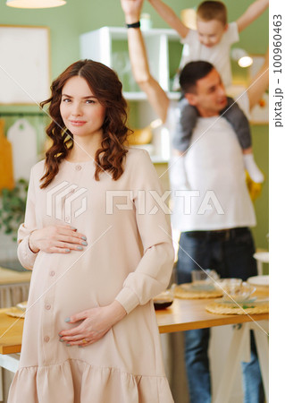 pregnant mom against the background of son and dad In the kitchen. pregnant mom against the background of son and dad In the kitchen. 100960463