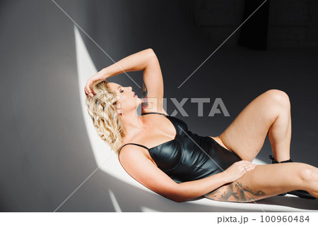 a portrait of a sexy blonde with tattoos in a leather swimsuit and boots. a portrait of a sexy blonde with tattoos in a leather swimsuit and boots. 100960484