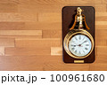 木の床を背景にした大きな鐘のついた金メッキの時計 100961680
