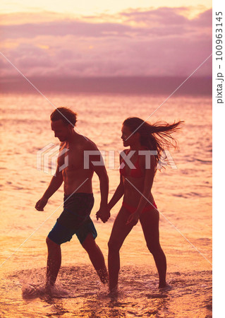 Beach couple walking on romantic sunset summer travel vacation silhouettes Sunset Caribbean tropical destination holidays woman and man young lovers relaxing on romance getaway 100963145