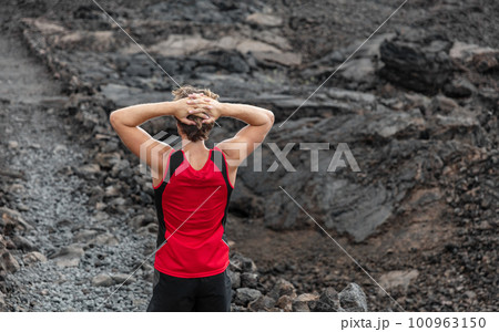 Tired runner exhausted on mountain trail run taking a break resting with back pain on black lava volcanic rocks path on outdoor summer Hawaii landscape 100963150