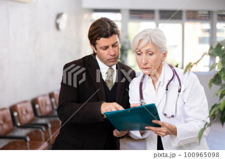 Adult man in suit and elderly woman doctor with folder of documents 100965098