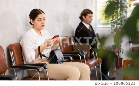 Young confident woman is sitting in the lobby of a large company, waiting for her turn to see a specialist in office 100965223