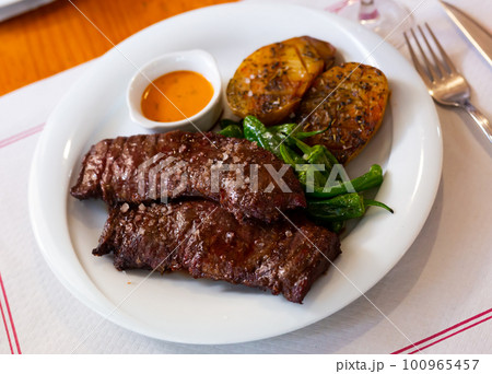 Grilled beef steak marinated in piquant chimmichurri with side dish of unpeeled baked potatoes Grilled beef steak marinated in piquant chimmichurri with side dish of unpeeled baked potatoes 100965457