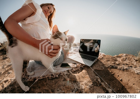Woman sea laptop. Business woman petting cat and working on laptop by the sea. Close up on hands of pretty lady typing on computer outdoors summer day. Freelance, digital nomad and holidays concept. 100967802