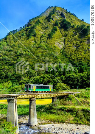 只見線　秋の真奈川橋梁を渡る列車キハE120形と蒲生岳(福島県只見町、10月) 100970586