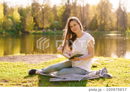 Young hipster girl enjoys sun and nice warm day reading book while relaxing 100970657