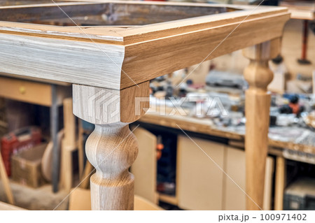 Wooden dining table with carved leg of solid oak and metal frame build process in workshop close up view 100971402