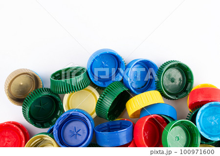 Multicolored plastic bottle caps are scattered on a white background. 100971600