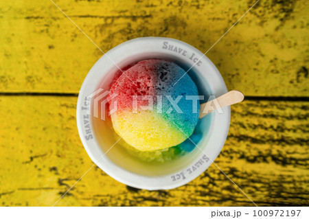 Shave Ice Hawaii local food hawaiian snow cone with three colors colored dyes. Frozen dessert food top view of bowl on retro yellow table. Shave Ice Hawaii local food hawaiian snow cone with three colors colored dyes. Frozen dessert food top view of bowl on retro yellow table. 100972197