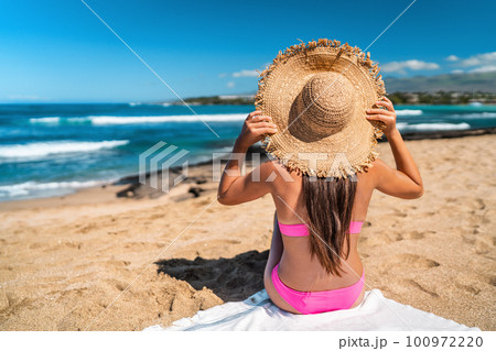 Beach girl in pink bikini wearing floppy hat sun tanning on Beach holiday in Caribbean destination sunbathing relaxing with view on ocean. 100972220