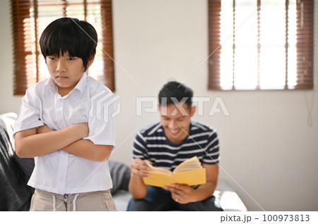 An angry Asian boy stands with his arms crossed, feeling lonely by his father An angry Asian boy stands with his arms crossed, feeling lonely by his father 100973813
