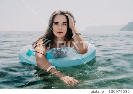 Woman summer sea. Happy woman swimming with inflatable donut on the beach in summer sunny day, surrounded by volcanic mountains. Summer vacation concept. 100974059