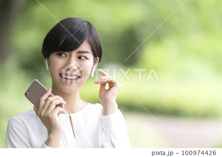 スマホで音楽を聴く若い女性　屋外 100974426