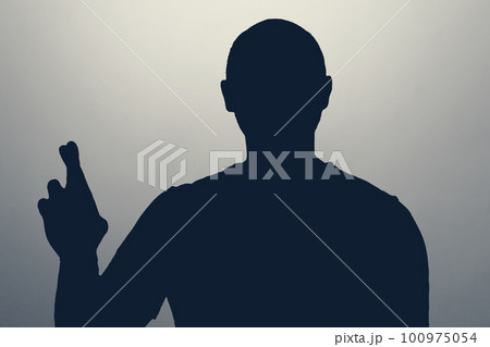 a male silhouette crosses his fingers begging for a drop of luck. a male silhouette crosses his fingers begging for a drop of luck. 100975054