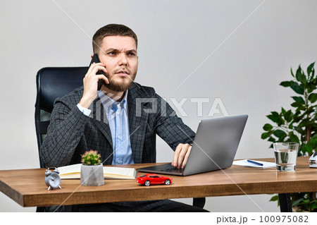 businessman sitting on chair at desk and talking on the phone businessman sitting on chair at desk and talking on the phone 100975082
