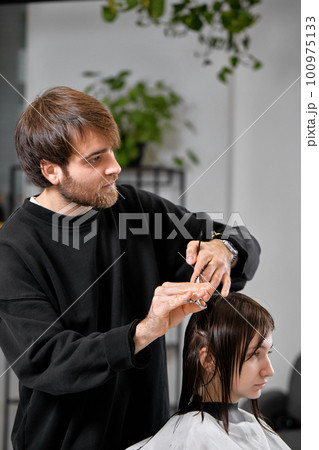 Professional male hairdresser cutting female hair in salon 100975133