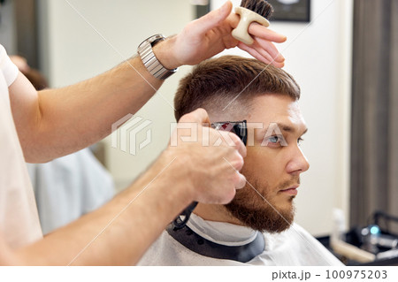 Barber trim hair with clipper on handsome bearded man 100975203