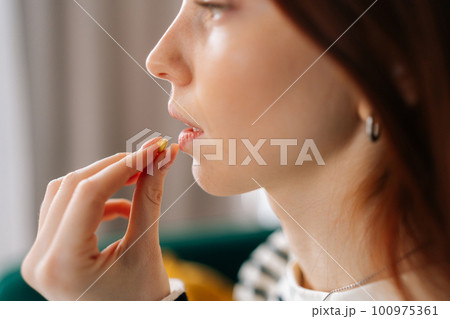 Close-up face of ill young woman taking pill. Closeup side view of sick redhead female holding medicament at mouth. Close up of depressed lady handing antidepressants tablet meds to mouth. 100975361