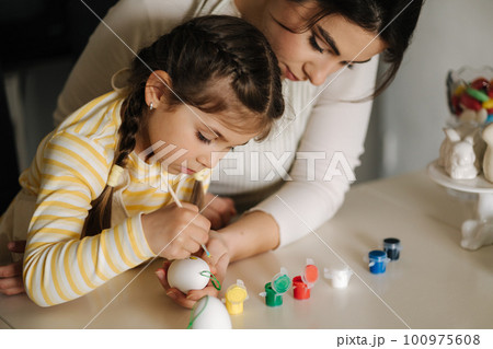 Portrait of mom and daughter painting easter eggs on kitchen. Spring holidays mood. Family 100975608