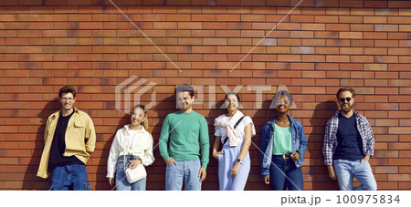 Diverse group of happy young men and women in casual clothes standing by street wall 100975834