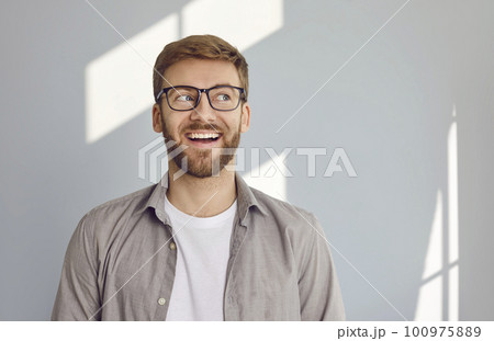 Portrait of smiling bearded man looking to the side on grey wall background. 100975889