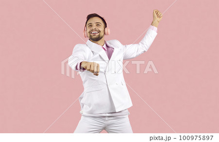 Positive excited handsome guy in white suit and headphones having fun on pink background. Positive excited handsome guy in white suit and headphones having fun on pink background. 100975897