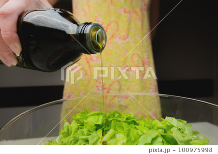 healthy eating, vegetarian food, dieting and people concept - close up of young woman dressing vegetable salad with olive oil at home 100975998