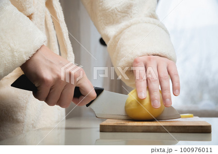 housewife cuts raw potatoes into small pieces with a knife. Close-up of hands while working in the kitchen. Cooking delicious breakfast or dinner 100976011