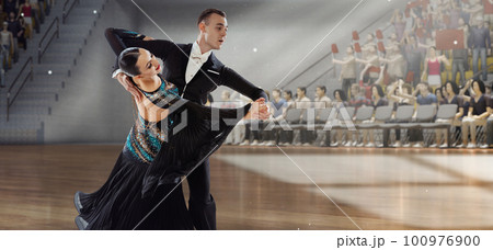 Graceful dancer. Young artistic man and woman in beautiful stage costumes dancing ballroom dance at stage under spotlights. Competition. 3D audience background 100976900