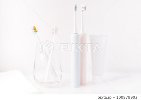 Children's toothbrushes in glass cup and electric toothbrushes against white background Children's toothbrushes in glass cup and electric toothbrushes against white background 100979903