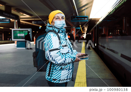 50s woman in face mask waiting on a train station platform with passport and tickets 50s woman in face mask waiting on a train station platform with passport and tickets 100980138