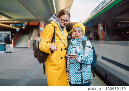 Portrait of one girl pointing the way to the train platform to another traveler woman at the walkway of train station in town 100980139