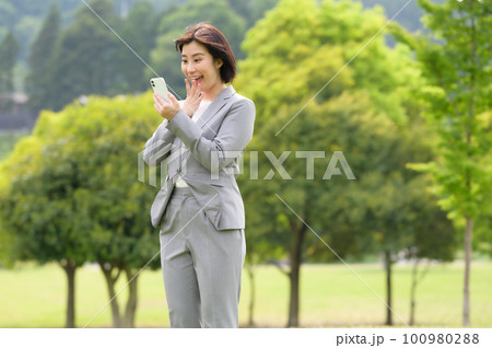 スマホを見て驚くビジネススーツの女性 100980288