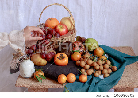 Dainty hand holding a grape over a table filled with bountiful fresh fruits 100980505