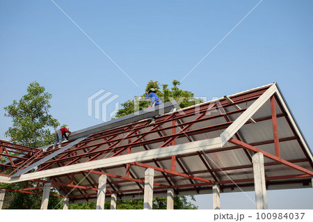 Roof repair, Construction worker installing new roof, roofing tools, power drill used on new roof with sheet metal. Roofing - construction worker standing on a roof covering it with metal. 100984037