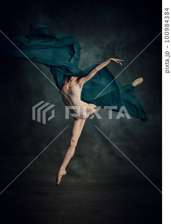 Weightless easy jump. Sensual ballerina with stretched feet dancing with fabric isolated over dark green background 100984384