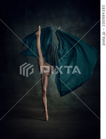 Young and incredibly beautiful ballerina standing in twine and holding silk fabric over dark green background 100984385
