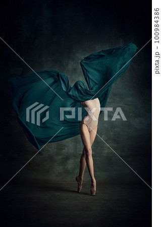 Shot of tender professional ballerina dancing in beige bodysuit with fabric isolated over dark green background 100984386