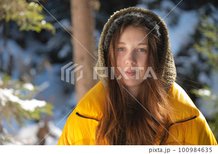 Winter walk through the forest, snow-covered beautiful pine forest. Portrait of a young lovely woman, she walks through the frosty nature and enjoys the winter weather 100984635