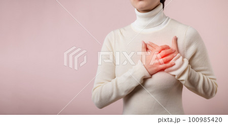 Young woman suffering from heart attack on light pink studio background. Painful cramps, Heart disease, Pressing on chest with painful expression. Healthcare world health day concept. 100985420