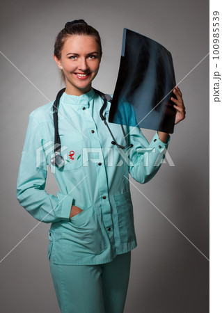 Young beautiful brunette doctor woman wearing stethoscope holding chest xray with a happy face standing and smiling with a confident smile showing teeth Young beautiful brunette doctor woman wearing stethoscope holding chest xray with a happy face standing and smiling with a confident smile showing teeth 100985539